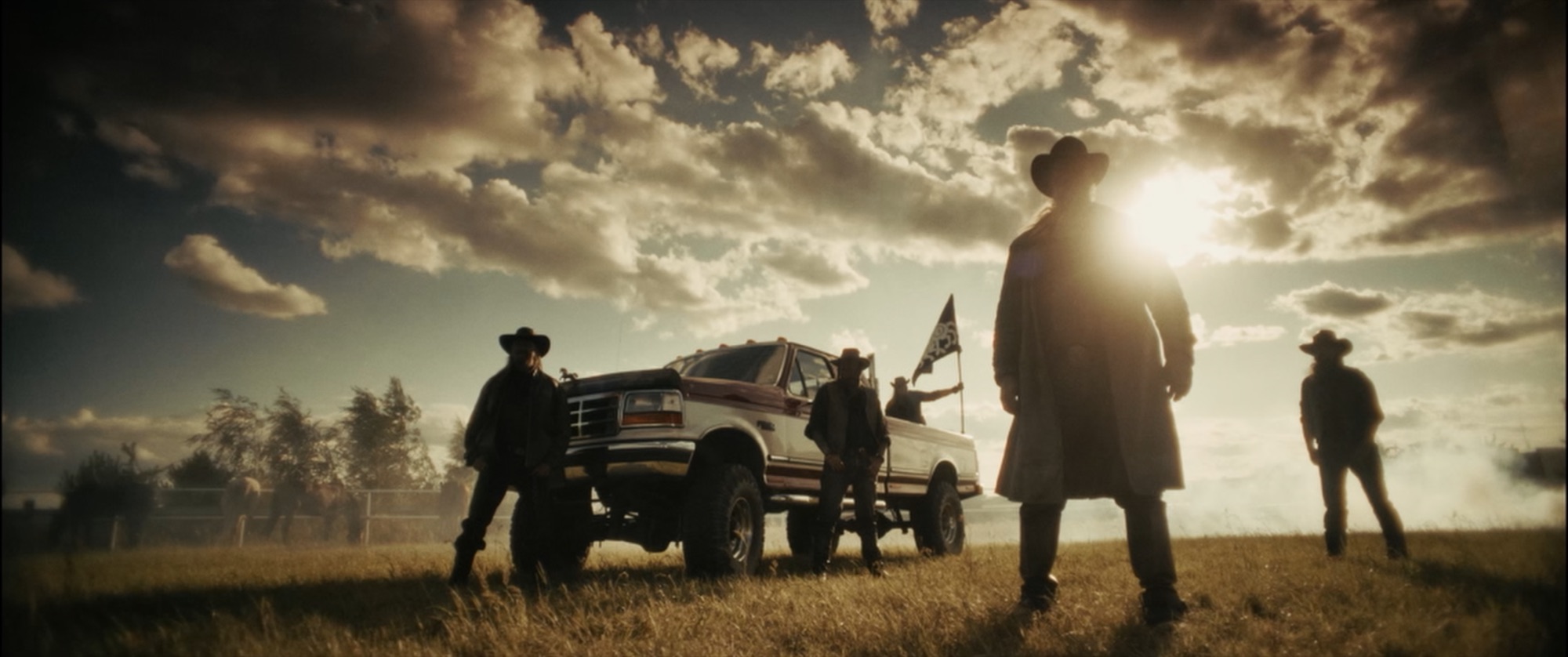 Silhouetted group of cowboys and a lifted pickup in a field against a dramatic sunlit, cloud-filled sky - Amon Amarth